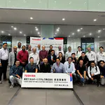 Teilnehmer des Global Distributor Meetings beim abschließenden Gruppenfoto nach der Werksbesichtigung bei TOSHIBA Energy Systems & Solutions Corporation. Vor ihnen ein Schild mit Firmenname, Standort und Datum: 18. Juni 2025.